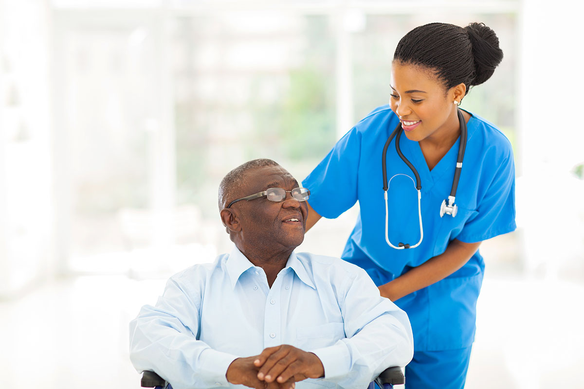 Older African American man in wheelchair being assisted by healthcare professional