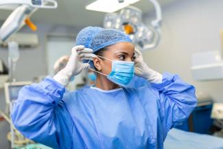 Portrait of female doctor surgeon putting on medical mask standing in operation room. Surgeon at modern operating room