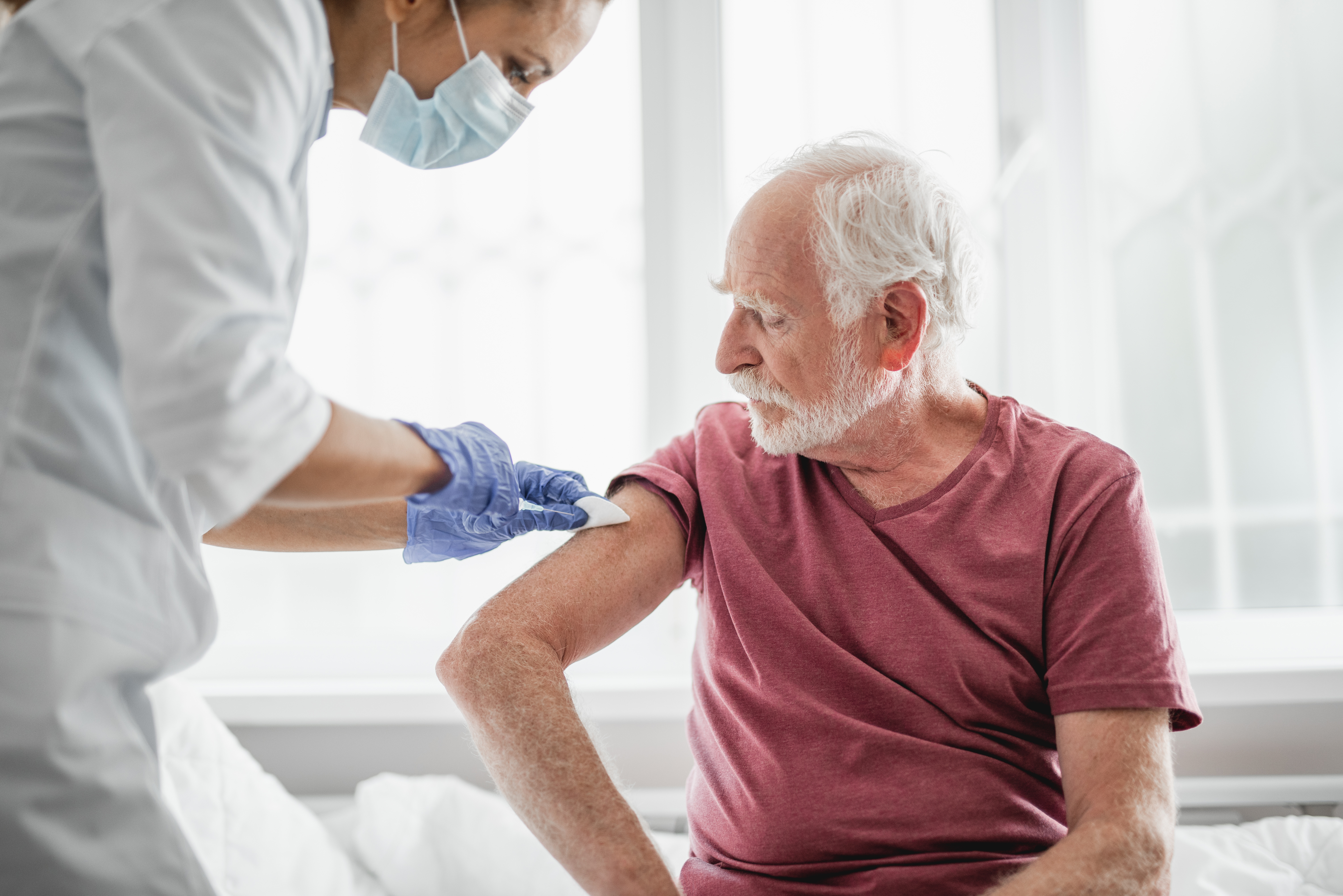 Image of health care worker preparing an older male patient's arm for vaccination.