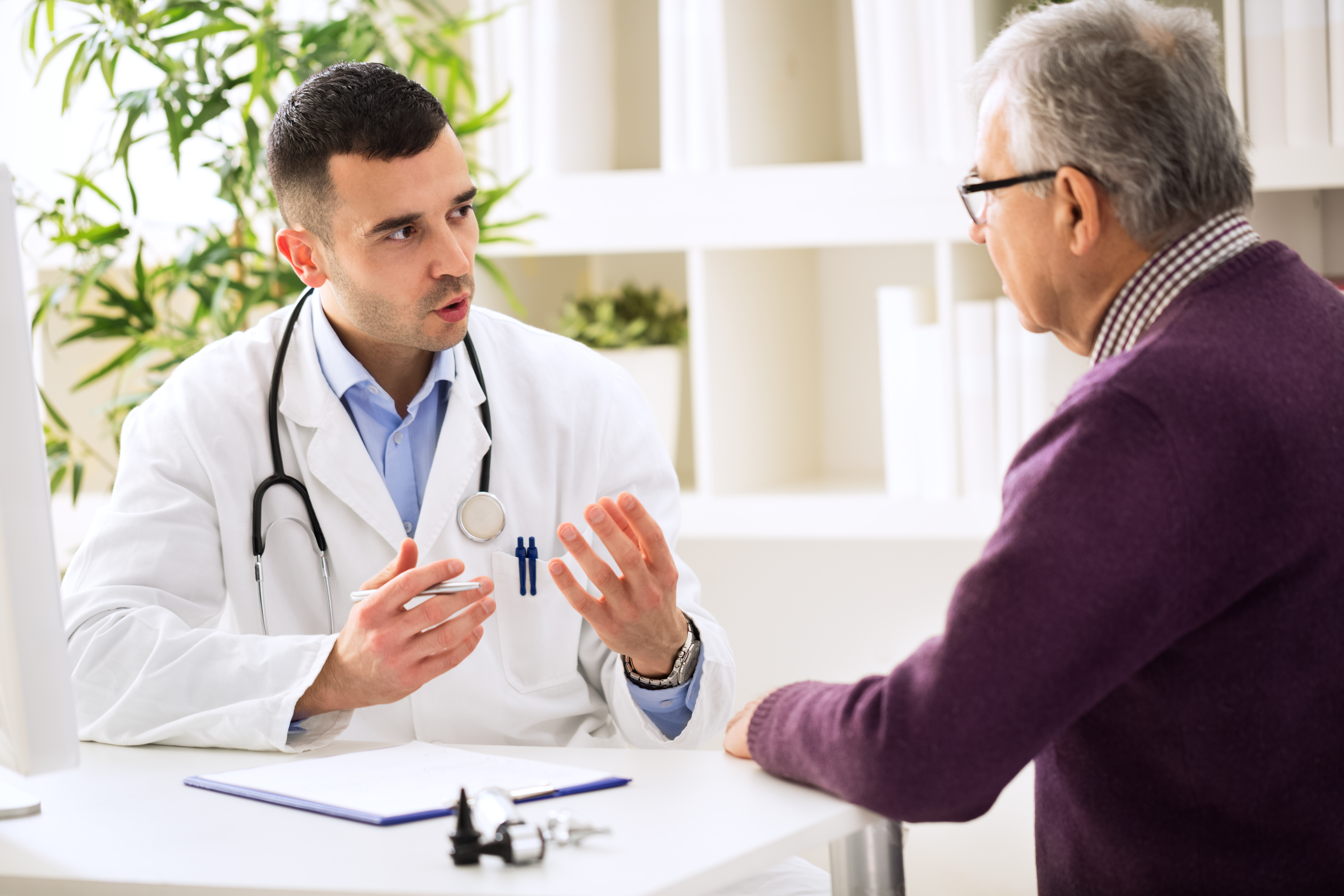 Image of a male doctor sitting across a table talking with an older man.