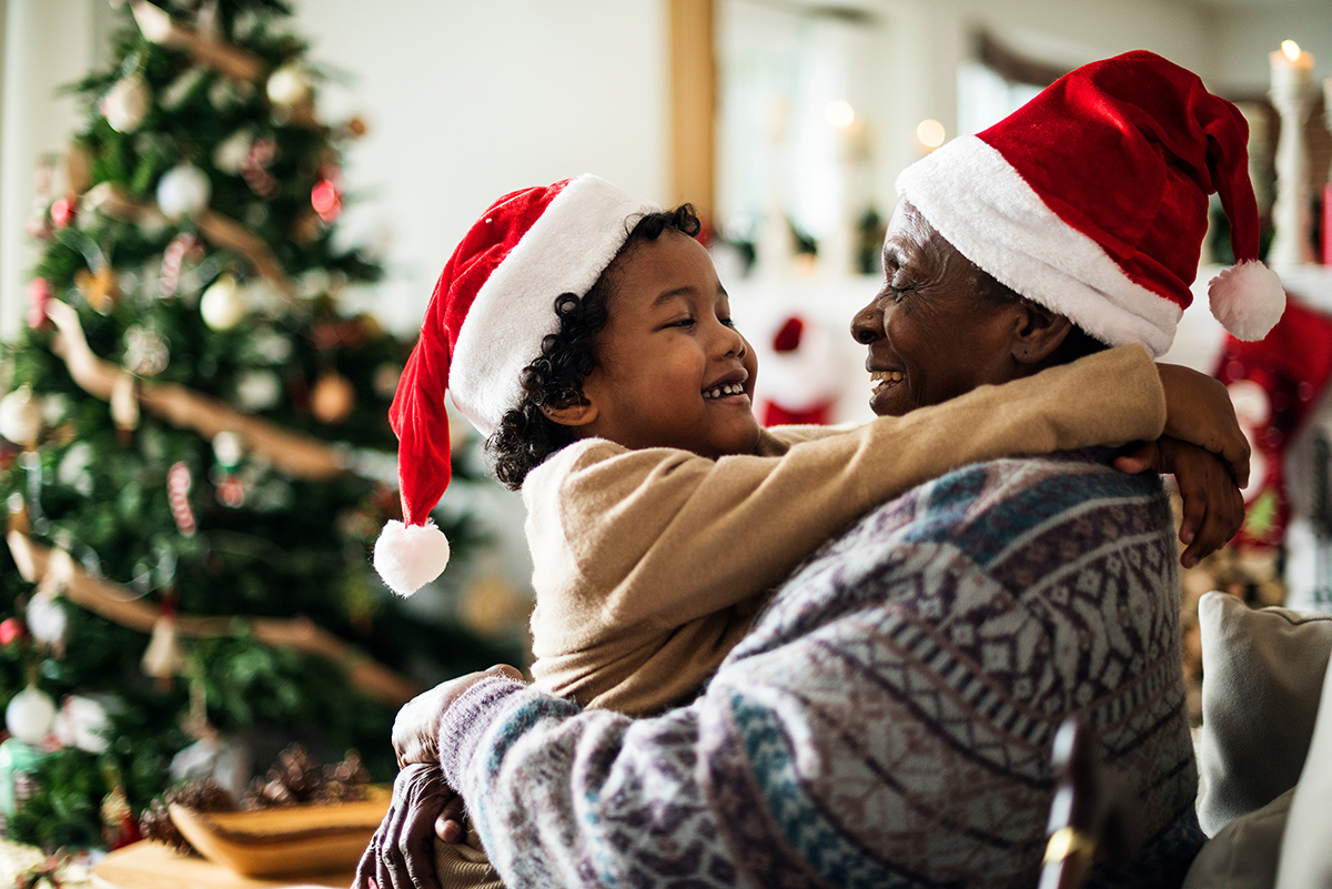 Image of young African-American male wearing a Santa hat with his arms around an older African-American man wearing a Santa hat.