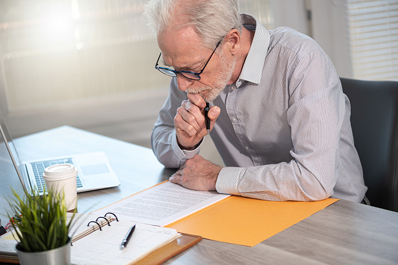 Image of older man reading documents at a desk.