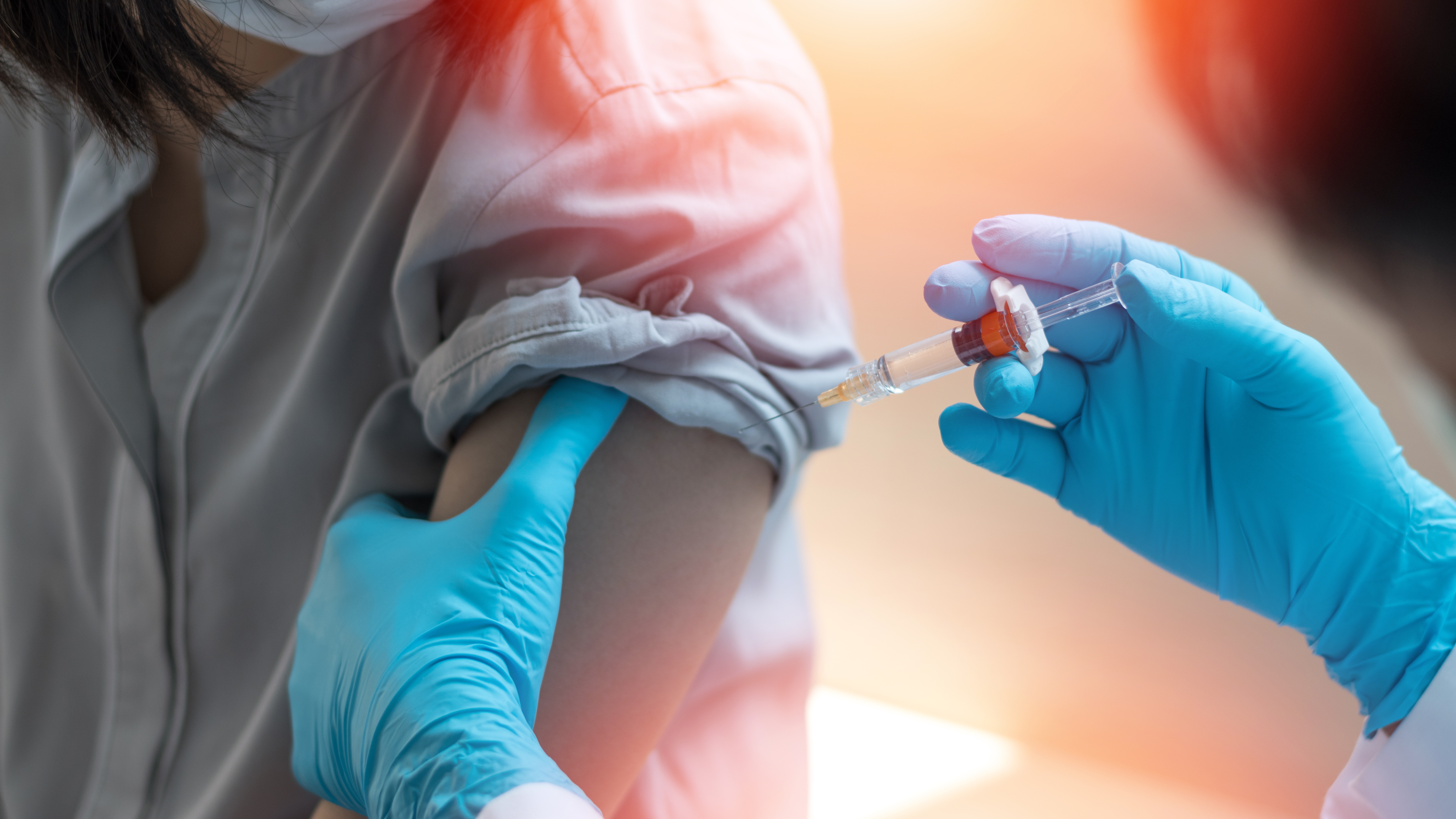 Image of blue gloved hands administering a vaccine to an arm with a rolled up sleeve.