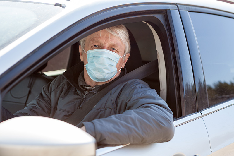 Image of older man wearing a mask and sitting in the driver's seat of a silver sedan.