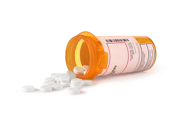 Image of a pill bottle on its side with round white pills spilling out