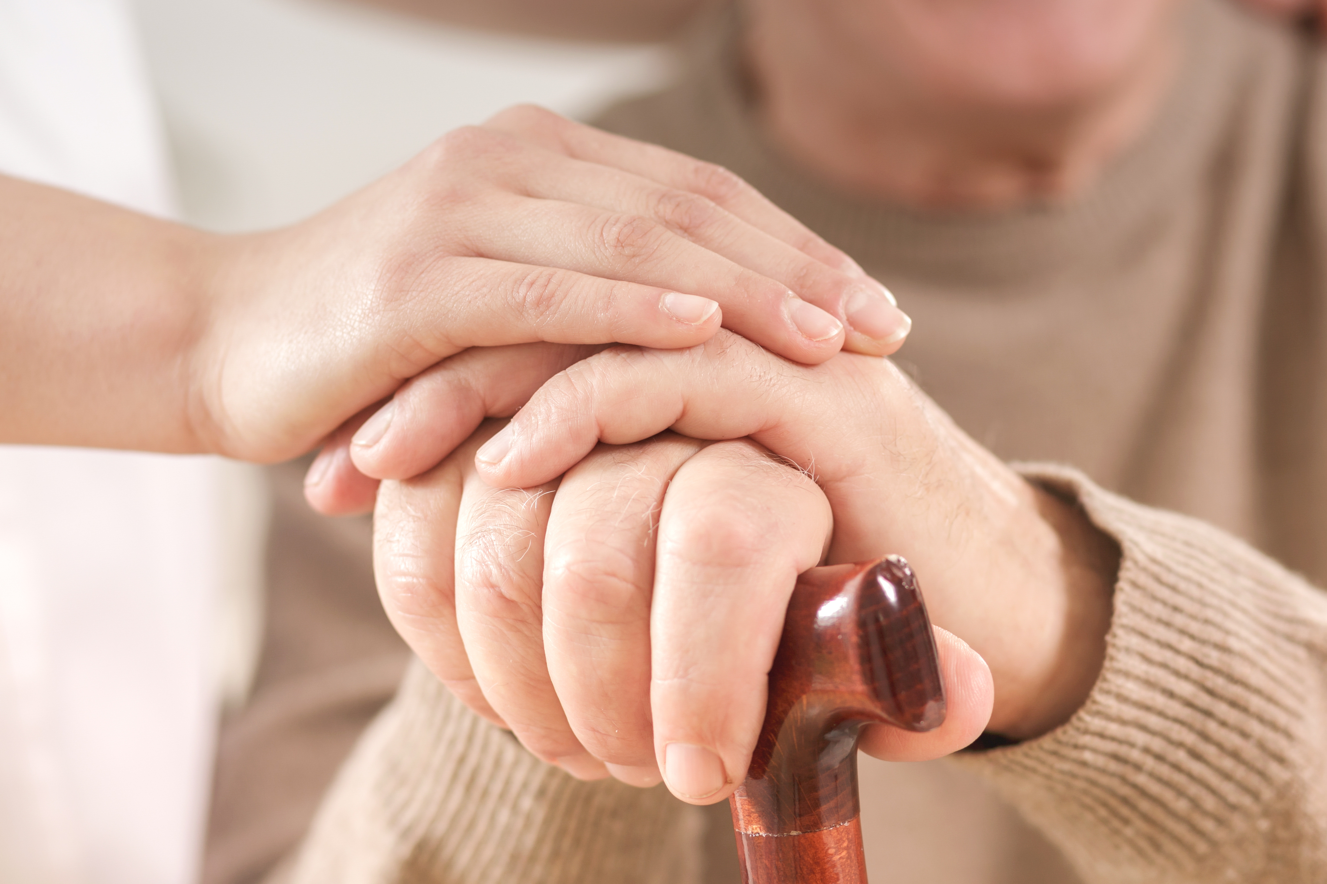 Close-up on senior person hand on walking stick and helpful caregiver