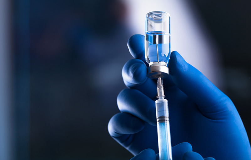 Image of a blue gloved hand holding a syringe that is being filled from a vaccine vial.