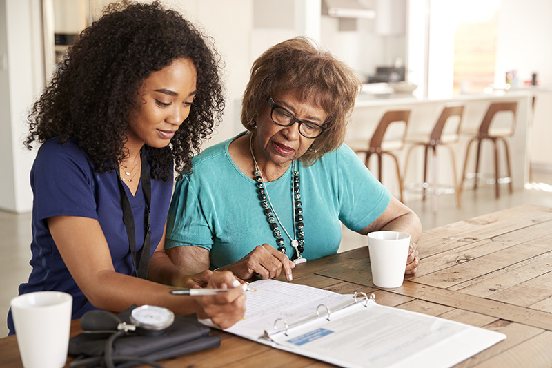 Image of a caregiver sitting next to a patient at the kitchen table reviewing a medical document.