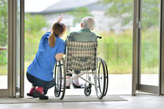 Image showing a health care worker kneeling beside an older man in a wheelchair as they look out two french doors.