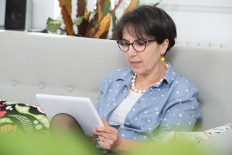 Image of older woman sitting on a couch looking at a tablet.
