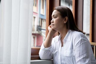 Image of middle age woman wearing a white shirt looking out a window 