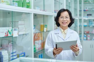 Woman pharmacist standing in front of cabinets of various prescriptions