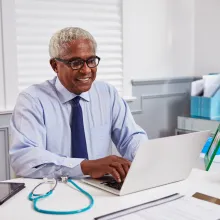 Senior black male doctor at work using laptop in an office