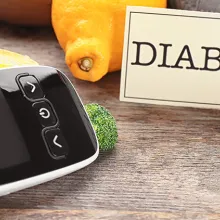 Digital glucometer, lancet pen and fruits on wooden background