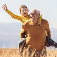 Grandfather carrying his grandson on his back in field