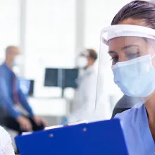 Disabled senior woman having a discussion with clinician in hospital hallway wearing face mask