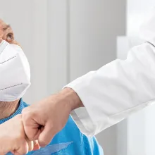 Female Senior adult with ffp2 mask is giving a doctor a fist bump
