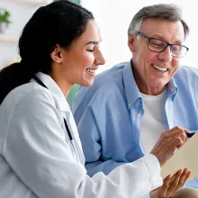 Young clinician asking senior impaired male patient in wheelchair to sign insurance policy at home