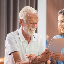 Asian nurse or caregiver teaching senior Caucasian man to handle with digital tablet computer at home