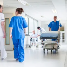 Male nurse pushing stretcher gurney bed in hospital corridor with doctors & senior female patient