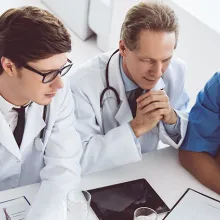 Two male and one female doctor and a male and female hospital staff in a discussion at a table.