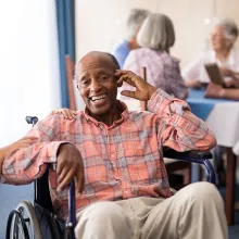 Female nurse in white jacket kneeling down next to male patient sitting in a wheelchair 