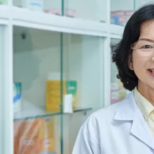 Female pharmacist in front of glass door with medications locked up.