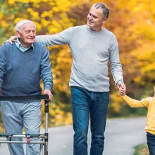 Older male with a walker walking with his son and grandson on a nice autumn day.