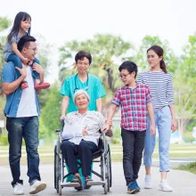 Caregiver moving male patient in wheelchair. Family is by his side.