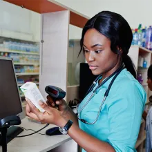 Pharmacy tech scanning box with a pharmacist is in the background