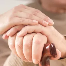 Image of clinician and patient hands. Patient hands are resting on a cane