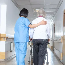 Asian doctor helping elder woman with walker in hospital hallway