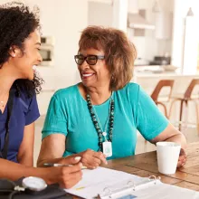 Female healthcare worker sitting at table smiling with a senior woman during a home health visit