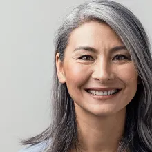 Asian woman with grey hair smiling standing near the wall