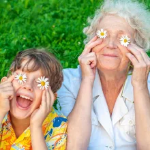 Happy grandmother and grandchild fooling around the lawn putting chamomiles on their eyes