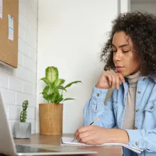 Young woman with curly hair writing notes on notepad 