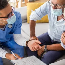 Male nurse talking to seniors patients with mask while being in a home visit.