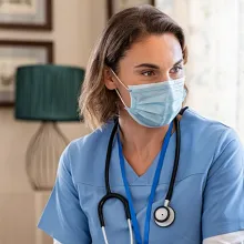 Female nurse with mask on sitting down with female elderly patient with mask on