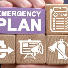 A man holding wooden blocks. Larger block states Emergency Plan. Smaller blocks have images of clipboard with plan checklist; house with an arrow pointing out; a siren and an axe and fire extinguisher.