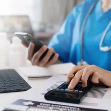 Healthcare professional using laptop and calculator at desk