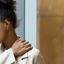 Female healthcare worker looking out window with hand on shoulder and showing a sign of burnout.