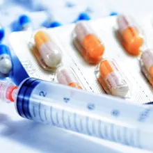 Image of medication tablets in a plastic bottle; packages medication capsules and syringe.