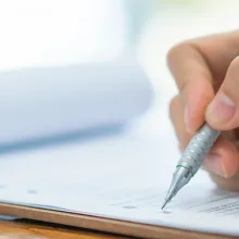 Image of a healthcare provider's hand filling out a form on a clipboard.