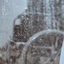 Image of a sad, elderly female looking out the window on a raining day.