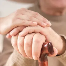 Image of healthcare provider putting their hands on top of an older adult (with a cane) hands. 
