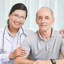 Image of a female healthcare staff putting their arms around a senior male resident. Both are smiling at the camera.