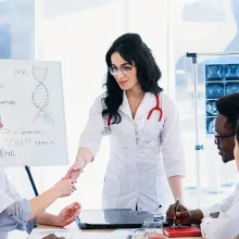 Image of clinicians sitting around a table while looking at another professional standing at a white board.