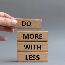 Image of a male hand putting together wooden blocks with the words 'Do More With Less'.