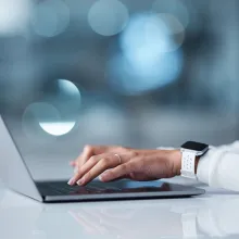 Female healthcare staff typing on a laptop in a healthcare setting.