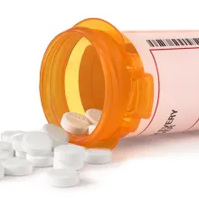 Image of a pill bottle on its side with round white pills spilling out